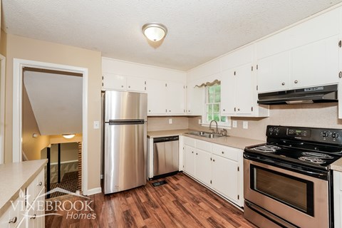 A kitchen with a stainless steel refrigerator, white cabinets, and a black stove top oven.