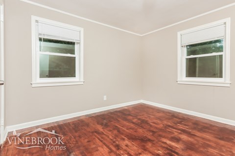 A room with wood flooring and two windows.