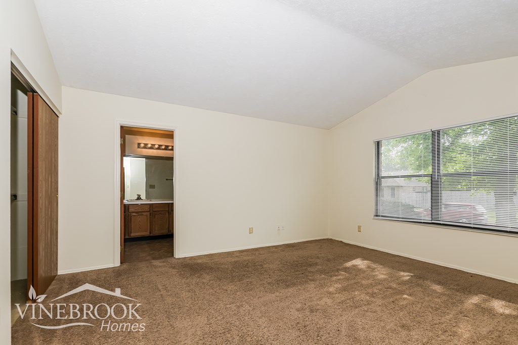 A room with a carpeted floor and a window with blinds.
