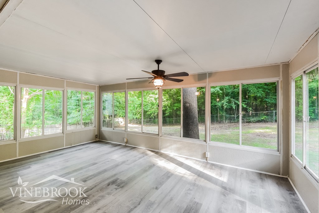 an empty living room with a ceiling fan and large windows