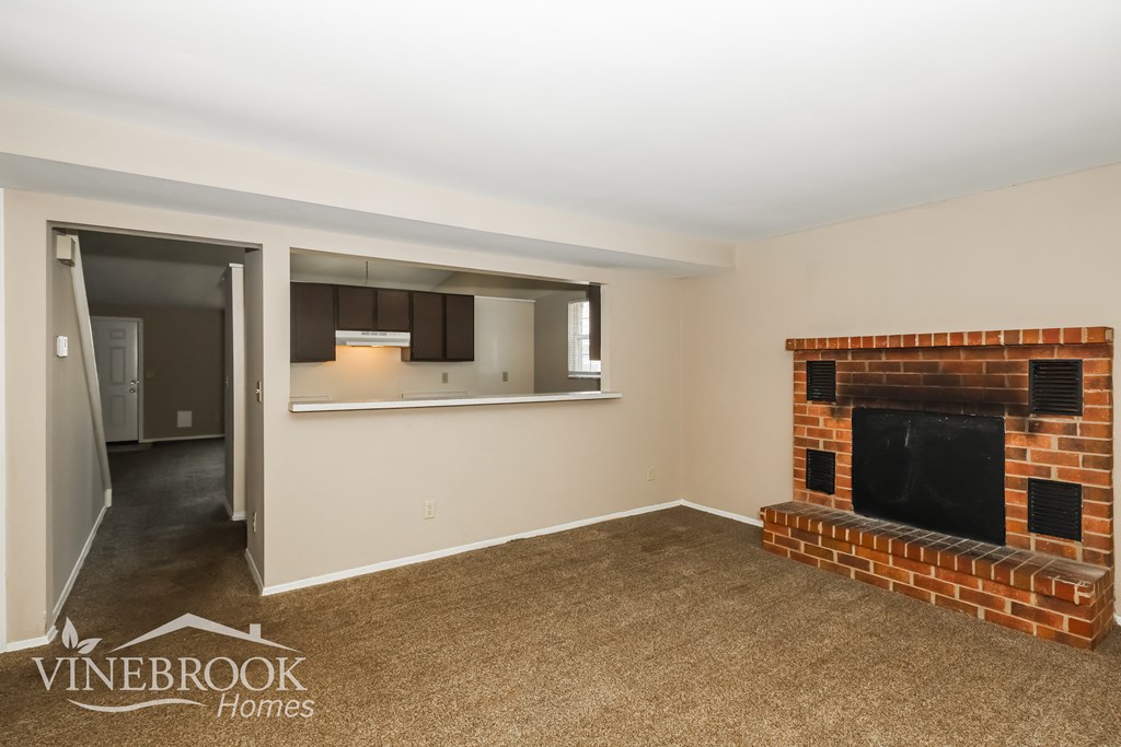 a living room with a brick fireplace and a kitchen