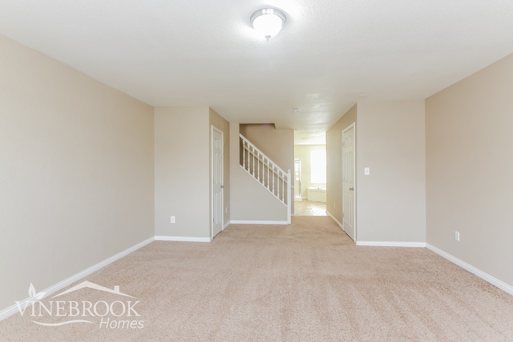 A spacious room with a carpeted floor and a staircase leading to another room.