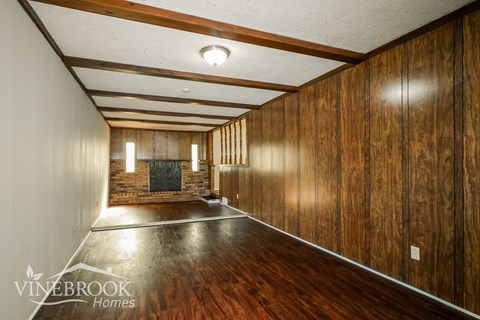 A long, narrow room with wood paneling and a fireplace.