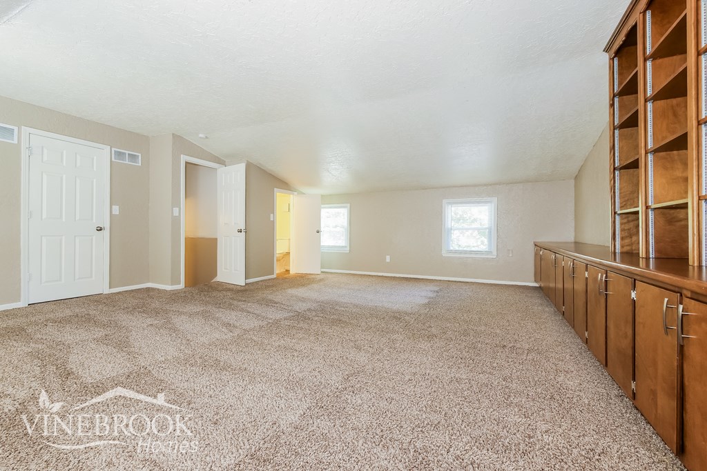 A spacious room with a carpeted floor and a row of wooden shelves on the wall.