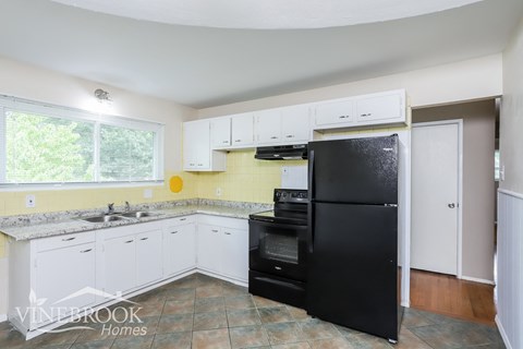 A kitchen with a black fridge and white cabinets.