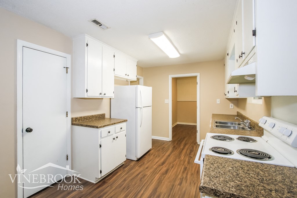 a renovated kitchen with white cabinets and appliances and a wood floor