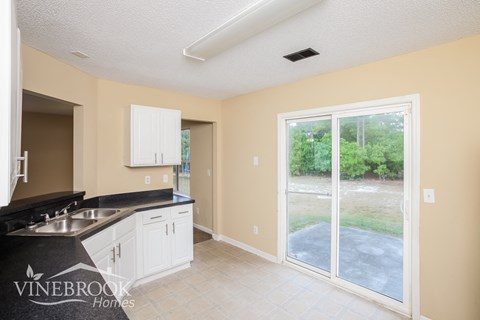 A kitchen with a sink and cabinets in a room with a sliding glass door.