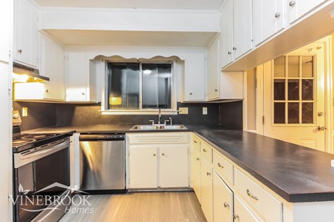 a kitchen with white cabinets and black counter tops and a window