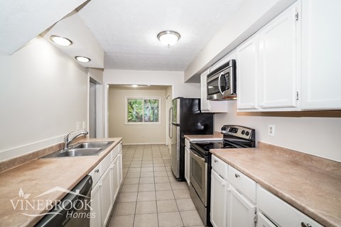 A kitchen with white cabinets and appliances, and a logo that reads "Vinebrook Homes".