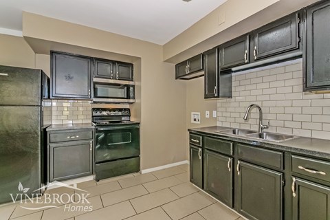 A kitchen with green cabinets and a black fridge.