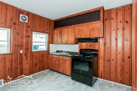 A kitchen with wooden walls and a black stove top oven.