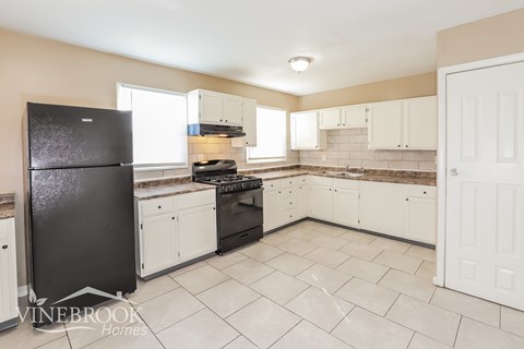 A kitchen with black fridge and white cabinets.