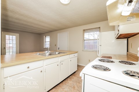 A kitchen with a white stove top oven and a sink with a faucet.