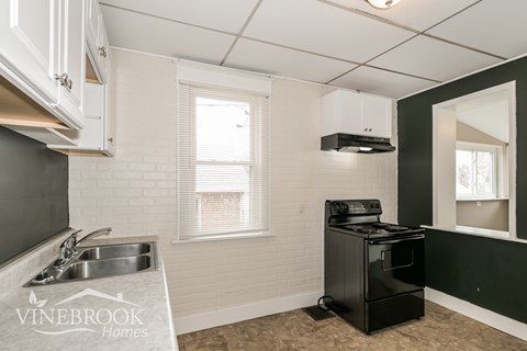 A kitchen with a black stove and a window with blinds.