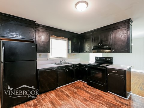 A kitchen with black cabinets and a wooden floor.