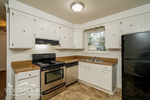 A kitchen with white cabinets and a black refrigerator.