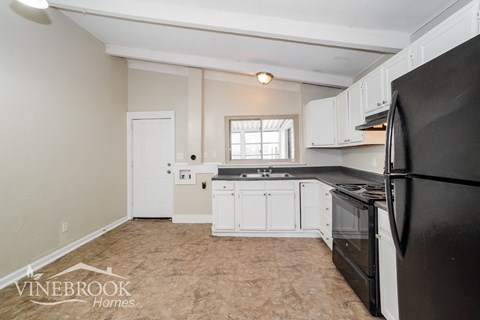 A kitchen with a black refrigerator and white cabinets.