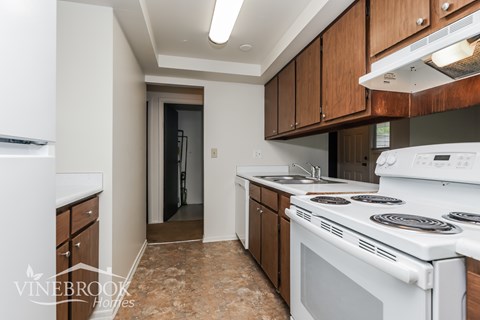 A kitchen with a white stove top oven and wooden cabinets.