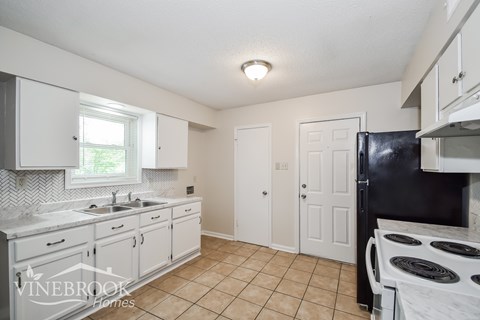 A kitchen with white cabinets and a black fridge.