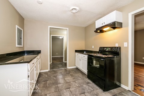 A kitchen with black appliances and a tile floor.