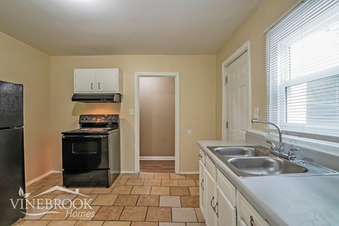 A kitchen with a black fridge, a black oven, a sink and a window.