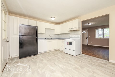 A kitchen with a black refrigerator, white cabinets, and a white stove top oven.