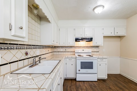 A kitchen with white cabinets and a white stove top oven.