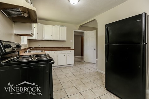 A kitchen with a black fridge and a black stove top oven.