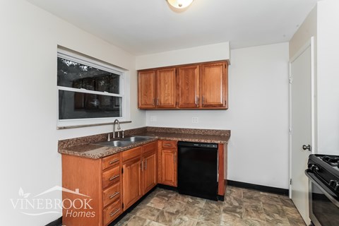 A kitchen with wooden cabinets and a black dishwasher.