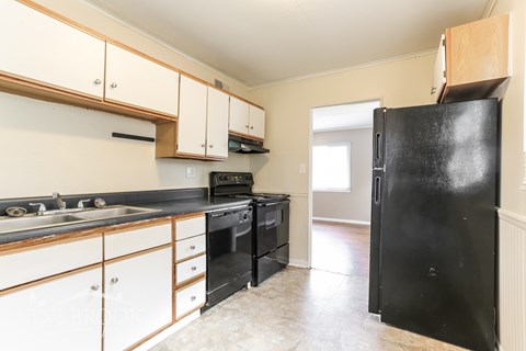 A black refrigerator stands in a kitchen with white cabinets and black appliances.