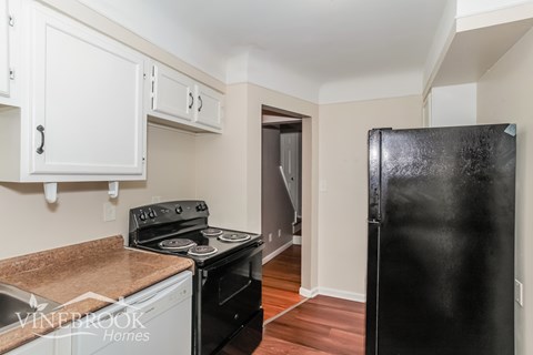 A black refrigerator is in the corner of a kitchen with white cabinets.