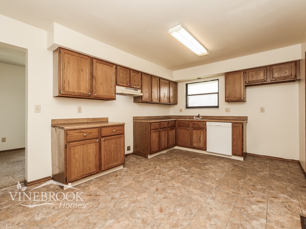 A kitchen with wooden cabinets and a white dishwasher is on the market.