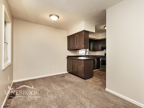 A kitchen area with brown cabinets and appliances in a room with carpeted flooring.