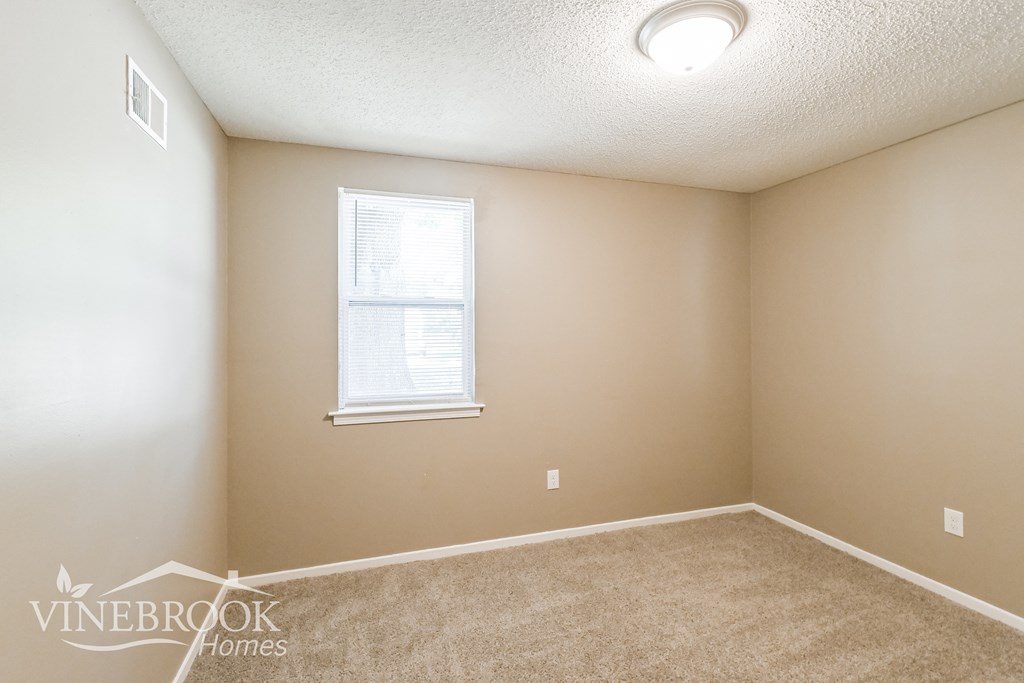 a bedroom with beige carpet and a window