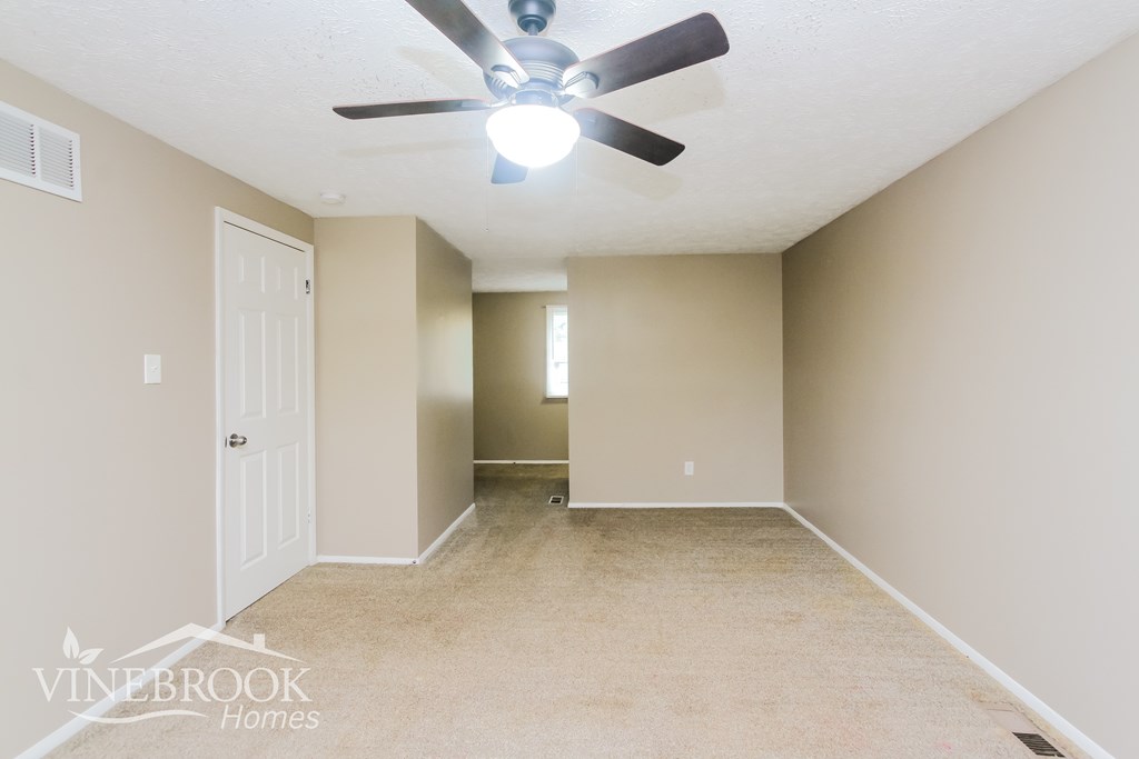 A room with a ceiling fan and carpeted floor.