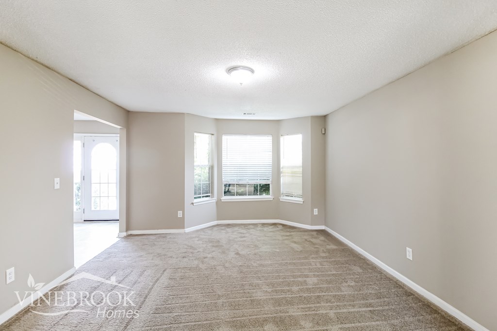 an empty living room with a rug and windows