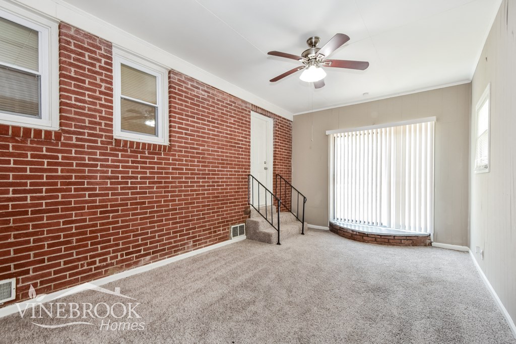 an empty living room with a brick wall and a ceiling fan