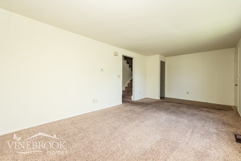 A room with carpeted floor and white walls, with a doorway leading to another room.