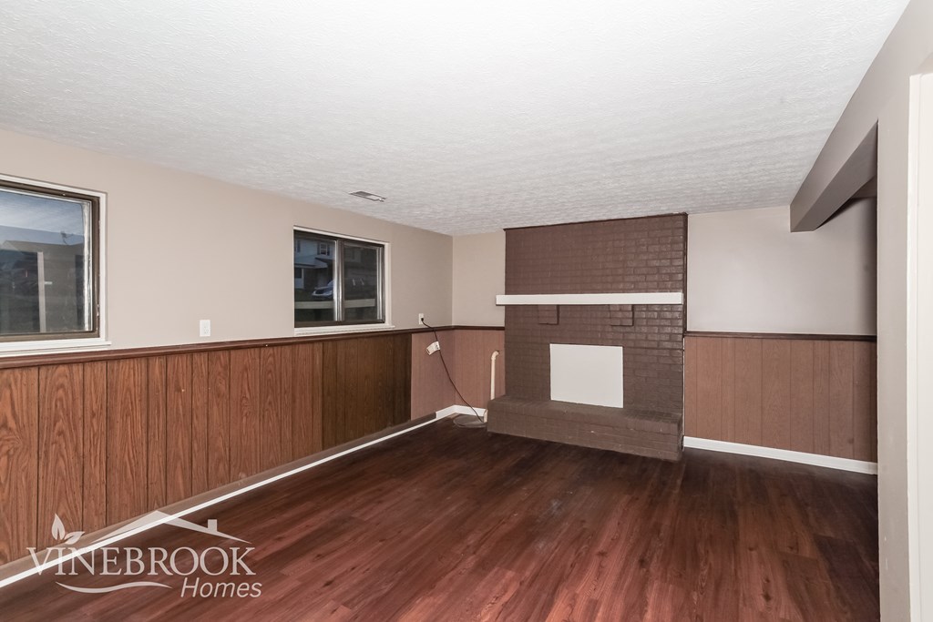 A room with wood flooring and a brick fireplace.