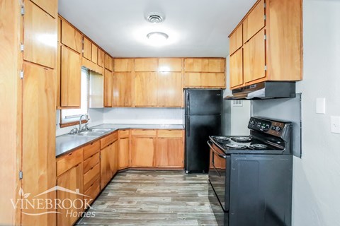 A kitchen with wooden cabinets and a black refrigerator.