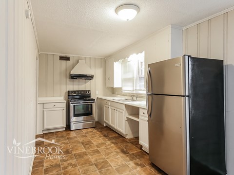 A kitchen with a black refrigerator and a tiled floor.