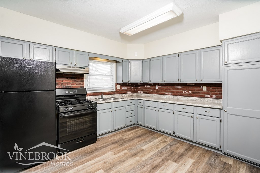 A kitchen with a black fridge and wooden floors.