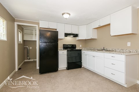 A kitchen with white cabinets and a black fridge.