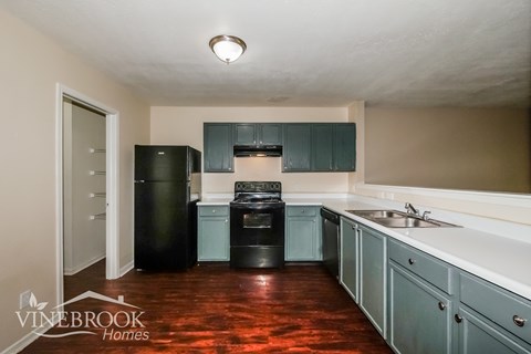 A kitchen with a black fridge and black dishwasher with a sink and a window.