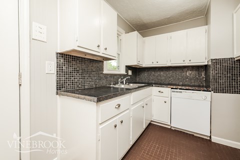 A kitchen with white cabinets and a black counter top.