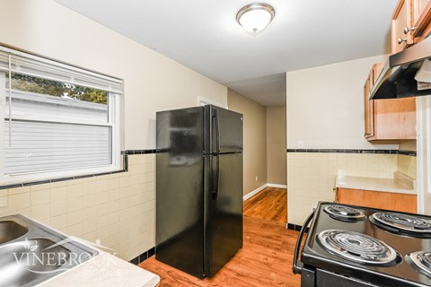 A black refrigerator in a kitchen with wood flooring.
