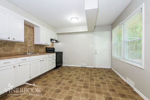 A kitchen with white cabinets and a brown tiled floor.