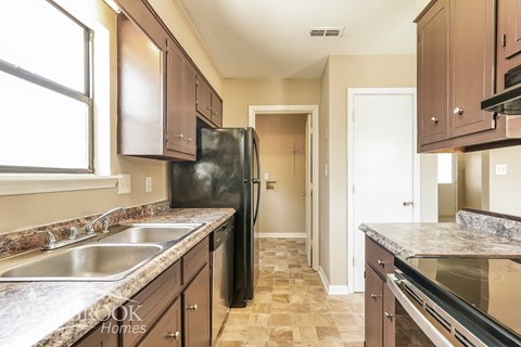 A kitchen with brown cabinets and a black refrigerator.