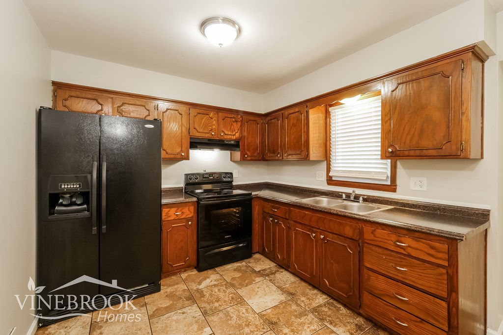 A kitchen with wooden cabinets and a black fridge.