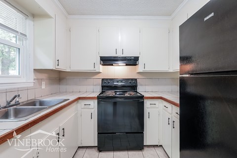 A black stove top oven in a kitchen with white cabinets.